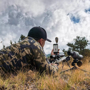 Sniper shooter using Tempest Weather Meter connected to smartphone to measure wind, temperature, and shooting conditions.